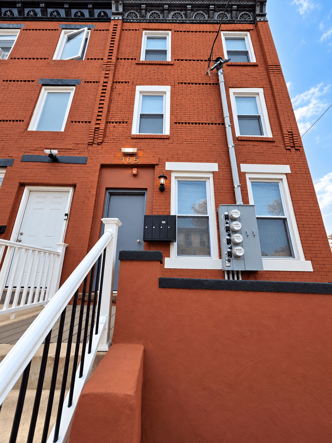 Daylight view of the brick rowhouse facade marked 105, with white window trim and entrance railings.